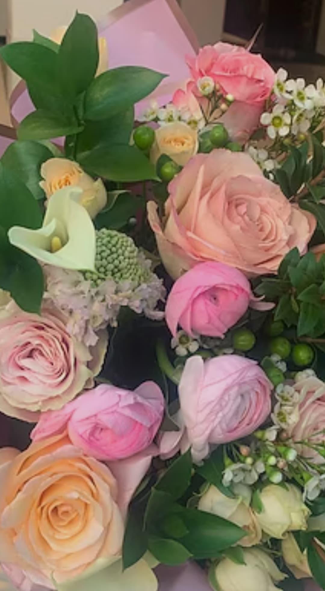 Vibrant bouquet of pink and peach roses, ranunculus, white calla lily, and lush green foliage.